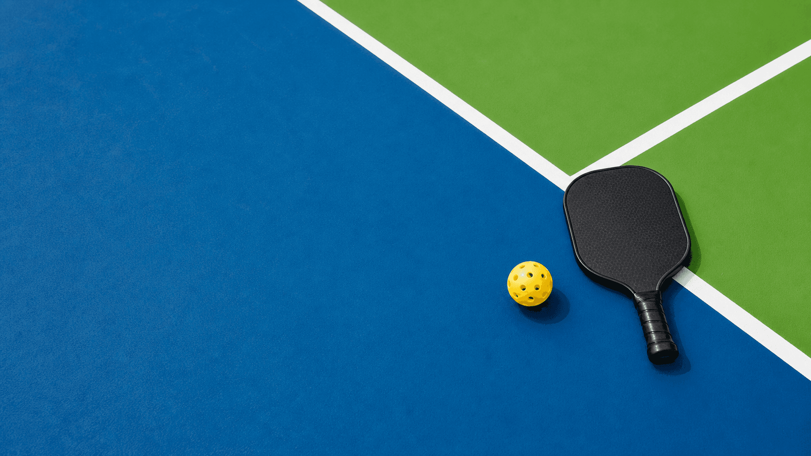 Pickleball court with paddle and yellow ball